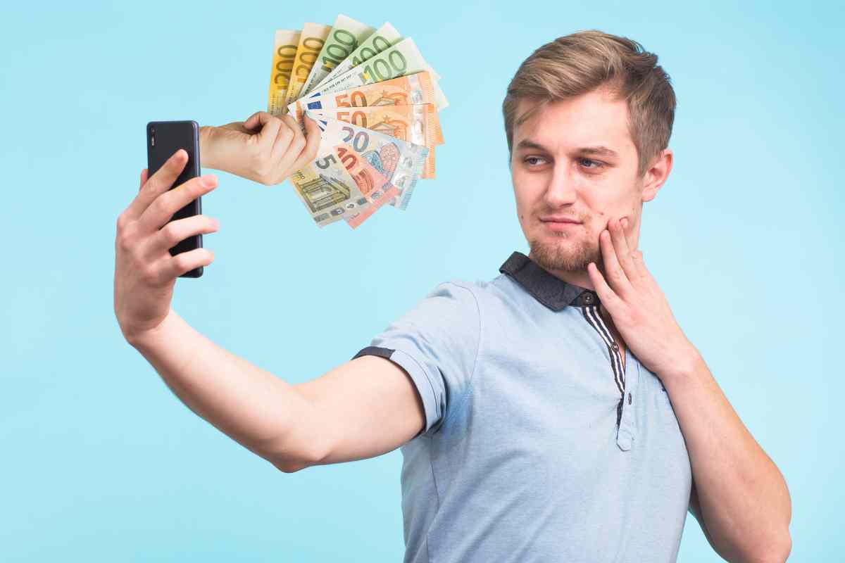 uomo si scatta un selfie e una mano esce dallo schermo con dei soldi