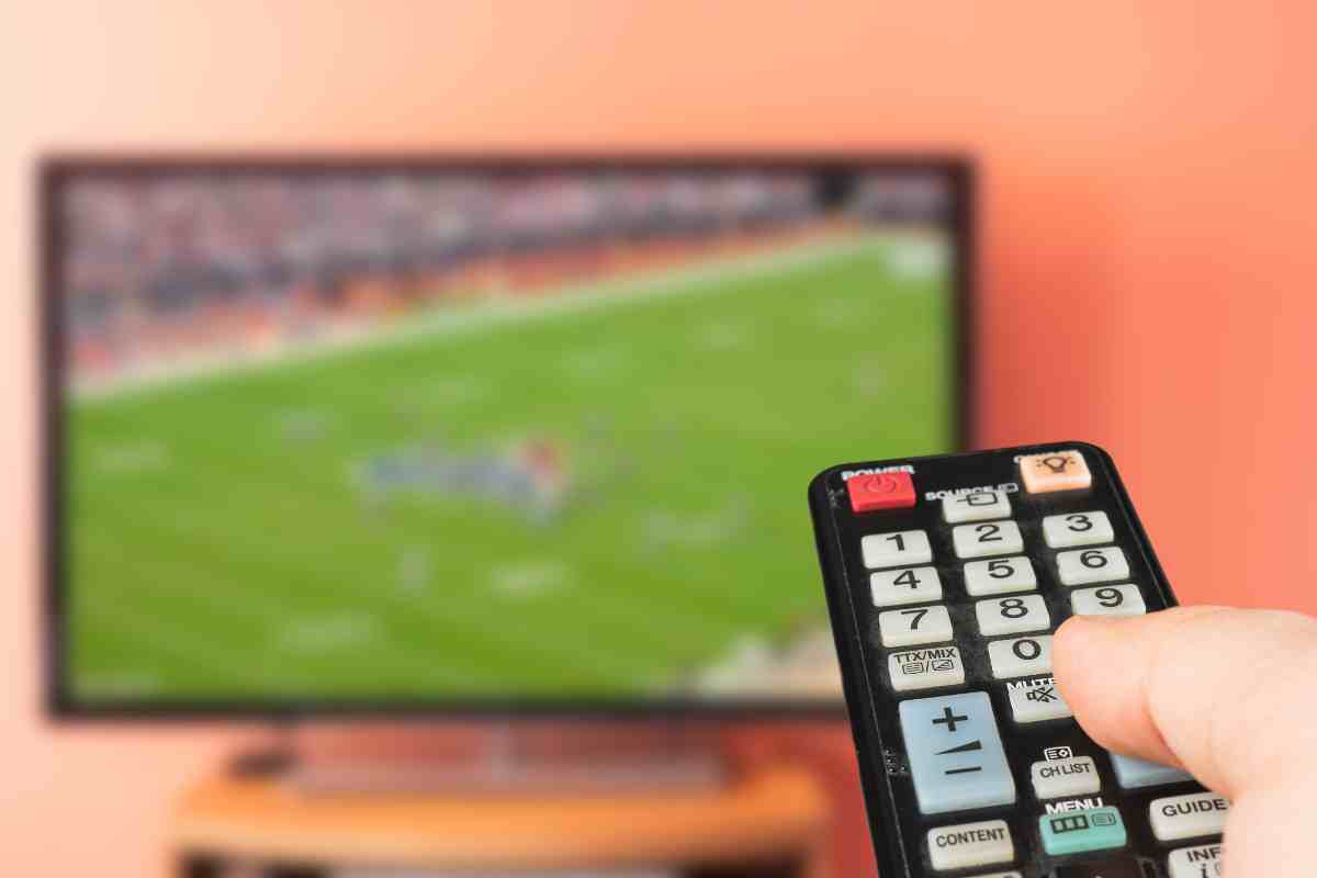 mano che usa telecomando e televisore con partita di calcio